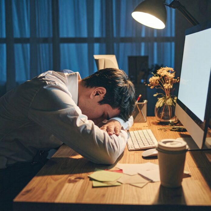 burnout-office-worker-late-night 늦은 밤 컴퓨터 화면 불빛만 남은 어두운 사무실에서 지친 직장인이 책상에 엎드려 번아웃과 만성 피로를 느끼고 있는 모습