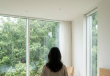 “서울에서 1시간?” 지친 나를 위한 선물, 주말에 가기 좋은 숲속 힐링 숙소 숲이 보이는 통창이 있는 현대적인 숙소 침대 위에서 편안하게 휴식을 취하고 있는 한국인 여성